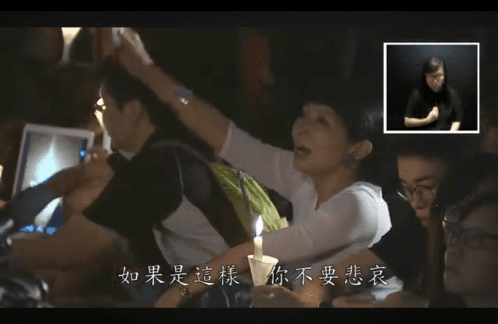 庭上播放 2018 年六四集會，大會唱〈血染的風采〉片段，畫面可見毛孟靜。（網上截圖）